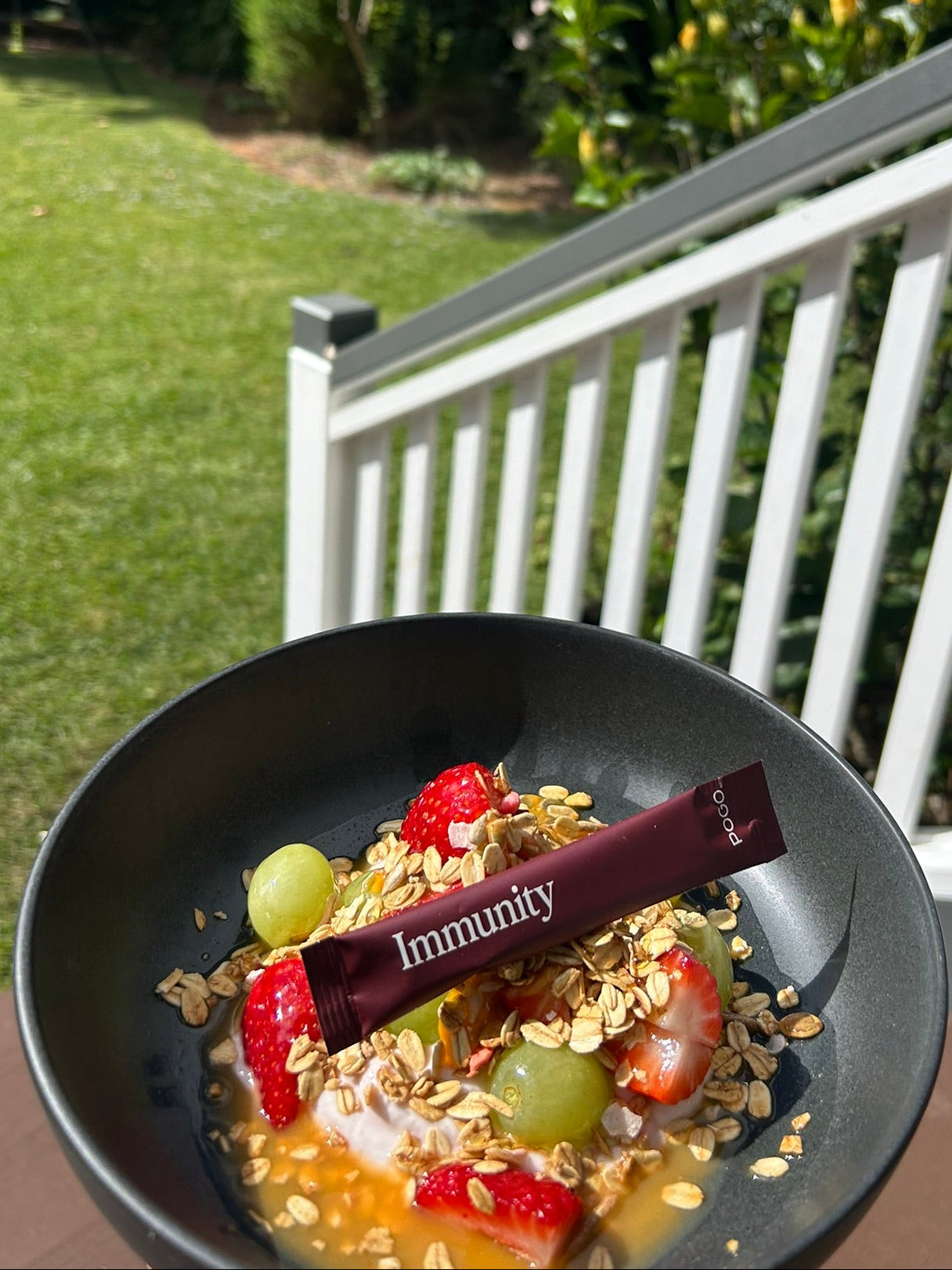 Fruit salad with a 'Immunity' bar on a black plate outdoors.